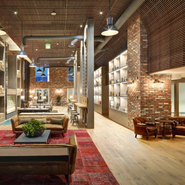 Hollywood, CA, Pet-Friendly Luxury Apartments - Vinyl Hollywood - Resident Lounge With Exposed Brick Walls, Wood Slat Ceiling, Leather Seating, Built-In Shelving, And Warm Pendant Lighting.