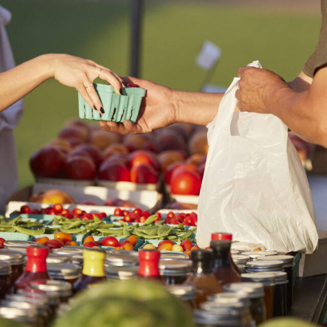 Farmer at market hands purchase to customer over colorful blend of organic produce